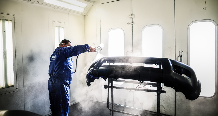 Technician refinishing a vehicle bumper inside an automotive paint booth