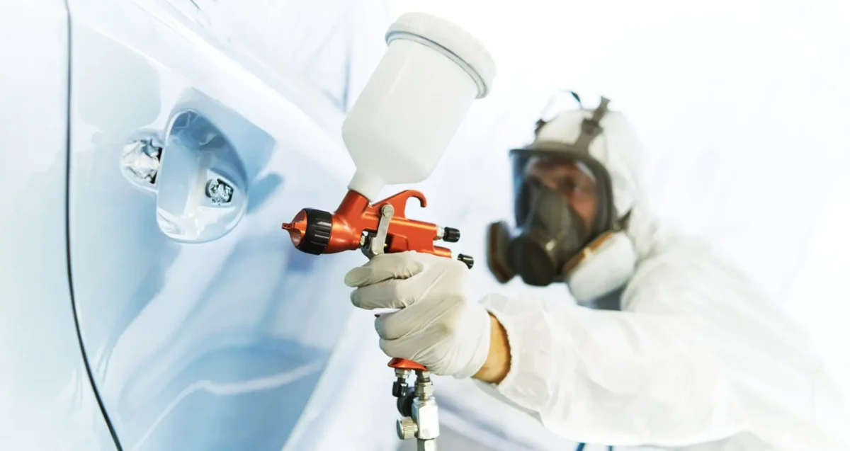 Technician applying paint refinishing to a vehicle during collision repair