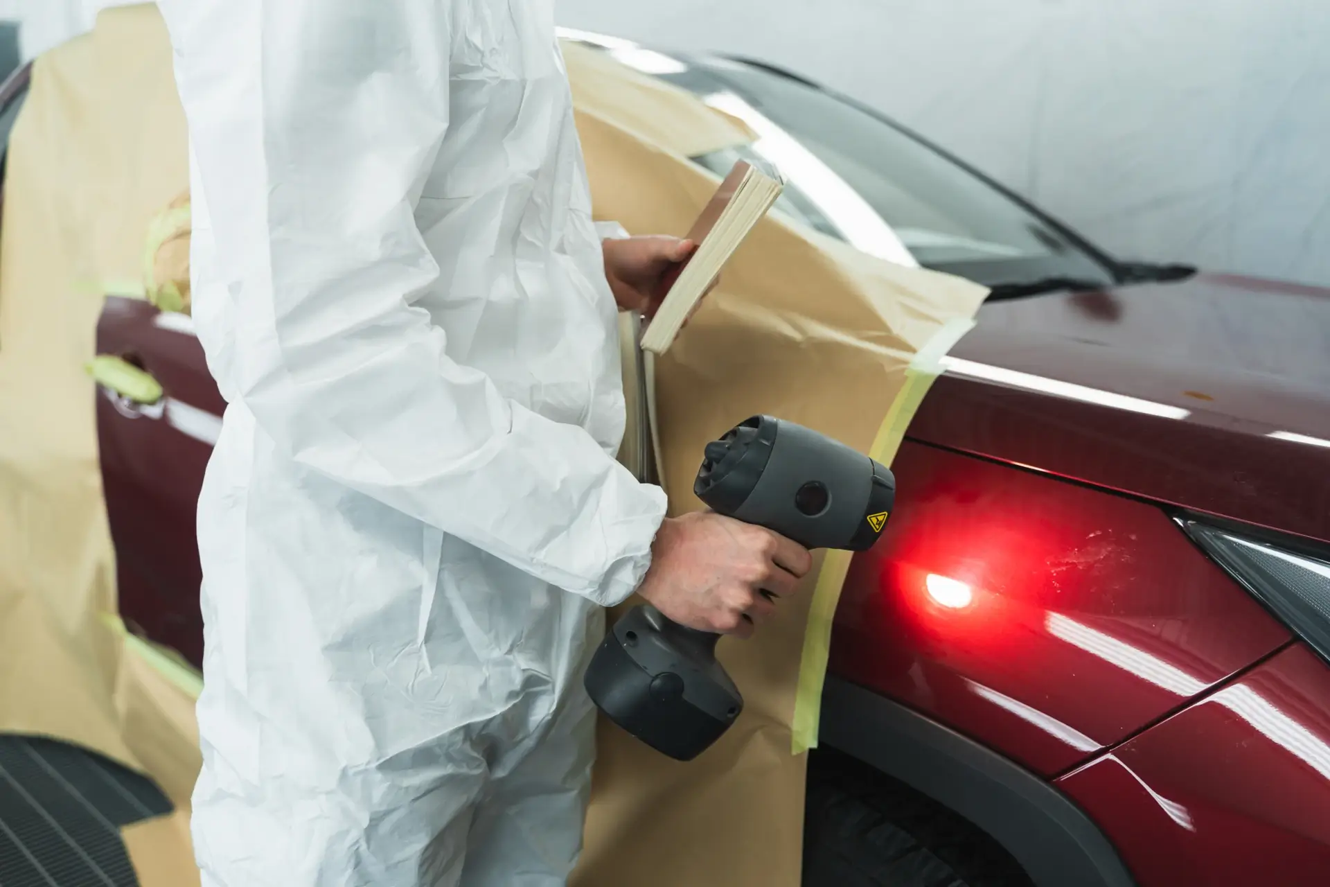 Technician checking paint color match on vehicle panel in auto body shop