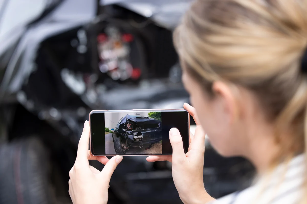 Driver taking photos of vehicle damage after a car accident